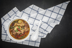 汤姆百胜泰国食物热辣的和酸红烧牛肉汤碗与白色陶瓷勺子和表格餐巾黑暗灰色的灰色黑色的语气纹理背景