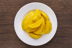 美味的新鲜的黄色的成熟的芒果简单的白色陶瓷板乡村自然木纹理背景前视图