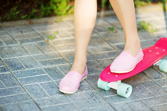 女孩站粉红色的滑板在户外特写镜头图像女脚滑板女脚运动鞋粉红色的滑板女孩游乐设施的沥青塑料滑板