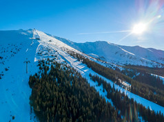 冬天斯洛伐克滑雪度假胜地明亮阳光明媚的天气滑雪山坡上的树木繁茂的山的太阳照明亮的蓝色的天空空中视图滑雪山坡上的度假胜地和的太阳空中视图