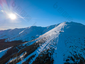 斯洛伐克滑雪度假胜地明亮阳光明媚的冬天天气滑雪山坡上的树木繁茂的山的太阳照明亮的蓝色的天空空中视图太阳和滑雪山坡上的度假胜地空中视图