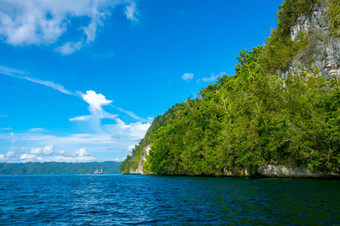 印尼岩石海岸热带岛阳光明媚的天气热带雨林坡航行船的距离岩石海岸与热带雨林和航行游艇