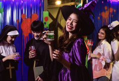 肖像年轻的女人沙拉酱万圣节服装享受和跳舞聚会，派对而喝和持有玻璃鸡尾酒与模糊背景人