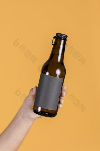 人类手持有棕色（的）啤酒瓶对黄色的墙背景高决议照片人类手持有棕色（的）啤酒瓶对黄色的墙背景