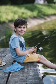 快乐男孩坐着木码头湖持有钓鱼杆