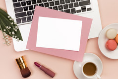 空白白色粉红色的纸移动PC与口红化妆刷咖啡杯与蛋白杏仁饼办公室桌子上