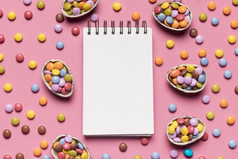 空白螺旋记事本包围与色彩斑斓的宝石糖果粉红色的背景