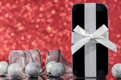 智能手机和装饰为圣诞节树黑色的玻璃表格在红色的背景焦点智能手机