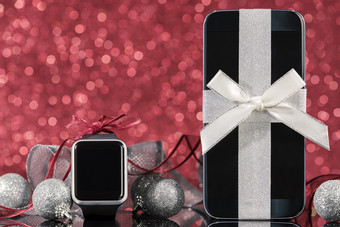 智能手机和智能手表和装饰为圣诞节树黑色的玻璃表格在红色的背景焦点智能手机