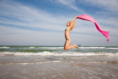 快乐美丽的女人跳与粉红色的披肩的海滩
