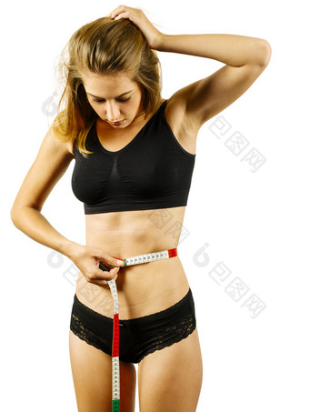 照片苗条的年轻的女人测量她的腰围在白色背景