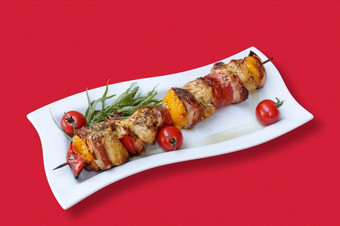 串肉和蔬菜的烧烤串肉和蔬菜的烧烤与西红柿和新鲜的草本植物红色的桌布
