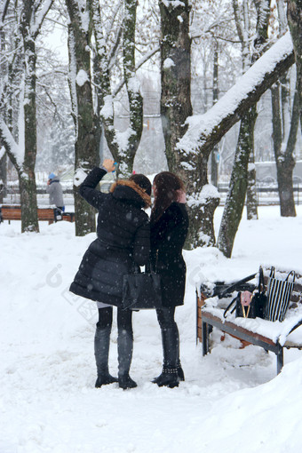 年轻的女孩使自拍背景雪冬天公园冻时间女孩冬天公园自拍现代女孩冬天公园在<strong>降雪</strong>女朋友取自拍智能手机冬天年轻的女孩使自拍雪冬天公园女朋友取自拍冬天