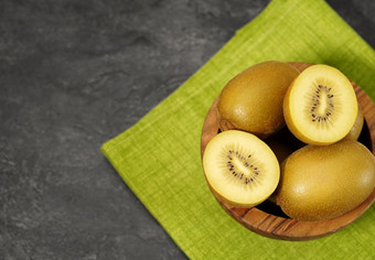 猕猴桃黄金黄色的水果木碗与一个切片猕猴桃灰色表格背景前视图与复制空间