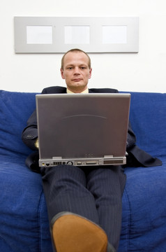 商人使自己舒适的沙发上与他的脚休息胸部同时工作他的移动PC