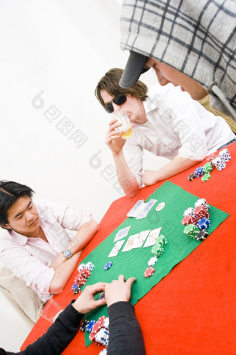 四个人坐着周围表格与红色的桌布为休闲游戏扑克