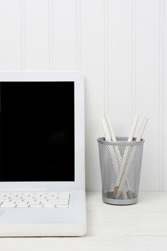 特写镜头首页办公室白色桌子上与移动PC而且铅笔杯的木桌子上前面白色beadboard墙的图像主要是阴影白色垂直格式与复制空间