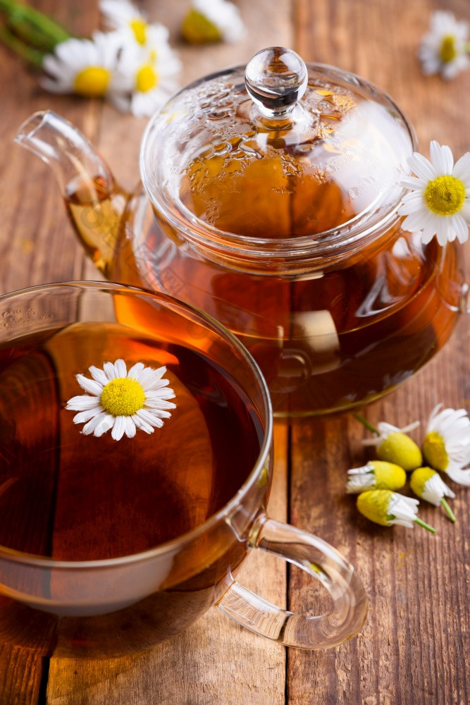 Herbal洋甘菊茶杯和玻璃茶壶与新鲜的洋甘菊草本植物古董木表格背景