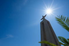 巨大的雕像基督的王通过绿色棕榈树叶清晰的夏天阳光明媚的一天里斯本葡萄牙与复制空间