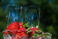 碗与新鲜的草莓与模糊香槟眼镜的背景花园