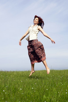 年轻的女人跳美丽的绿色草地