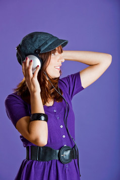 美丽的和快乐年轻的女人听音乐与耳机在紫罗兰色的背景