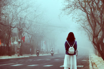 令人惊异的场景早期早....与女孩穿背包站看向前雾多雾的街与花瓣从行白色花沿着路年城市越南南