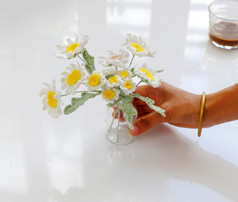 女人手持有手工制作的花能为首页装饰白色花瓣黛西和黄色的雄蕊用钩针编织从纱休闲活动白色背景