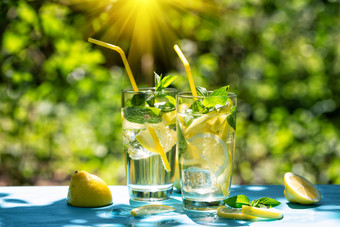 柠檬水和柠檬蓝色的表格对的背景绿色树叶的热夏天柠檬水和柠檬蓝色的表格