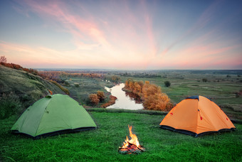 野营从的橙色和绿色帐篷与火的银行的河早期早....夏天景观概念旅行和孤独野营从橙色和绿色帐篷与火银行河
