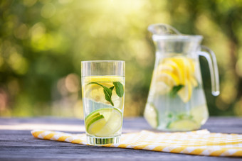 投手和玻璃自制的柠檬水木表格绿色自然背景的明亮的夏天太阳有机食物概念投手和玻璃自制的柠檬水木表格