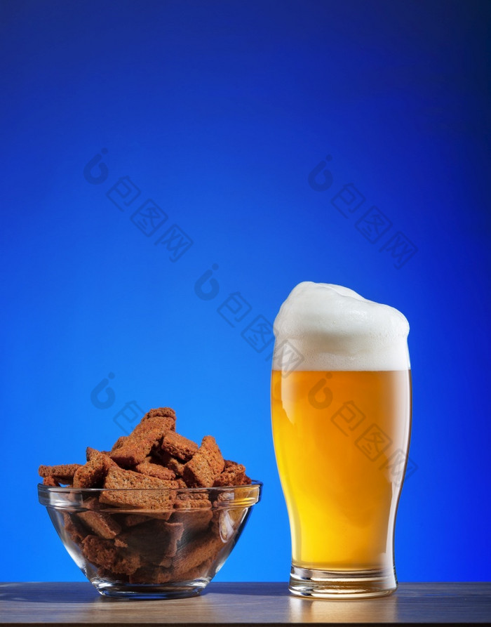 玻璃光啤酒和咸黑麦饼干蓝色的背景啤酒和零食木表格玻璃光啤酒和咸黑麦饼干