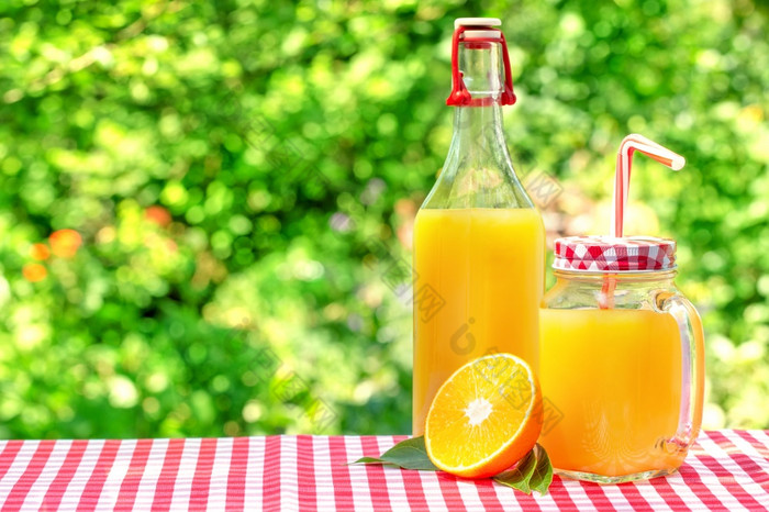 玻璃Jar和瓶与橙色汁一半橙色与叶子自然绿色背景玻璃Jar和瓶与橙色汁