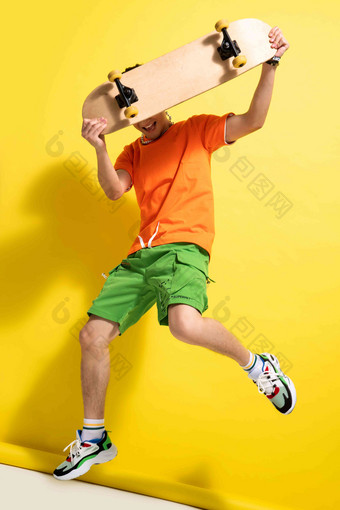 举着滑板跳跃的青年男人