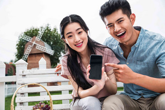 青年伴侣坐在户外展示手机
