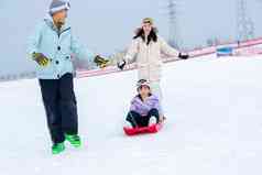 滑雪场上父母和坐在雪上滑板的女儿玩耍