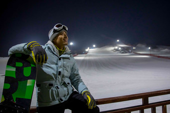 夜晚青年男人坐在滑雪场内的护栏上