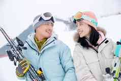 雪场上抱着滑雪板对视的快乐情侣