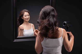 中年女人对着镜子用吹风机吹头发