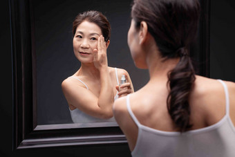优雅的中年女人对着镜子涂抹爽肤水