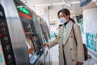 戴口罩的年轻女人在地铁站使用自动售票机