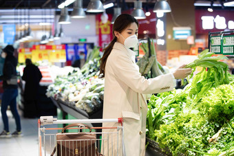 戴口罩的青年女人在超市挑选青菜