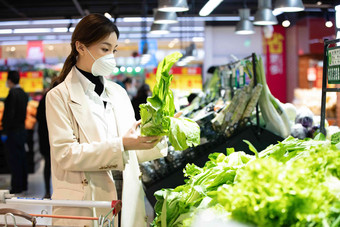 戴口罩的青年女人在超市购买青菜