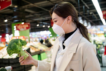 戴口罩的青年女人在超市购买蔬菜