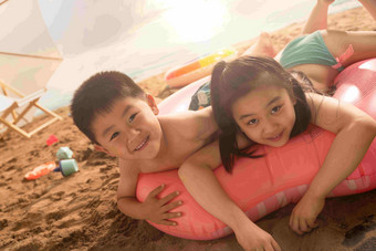沙滩上的快乐东方儿童<strong>趴在</strong>游泳圈上玩耍