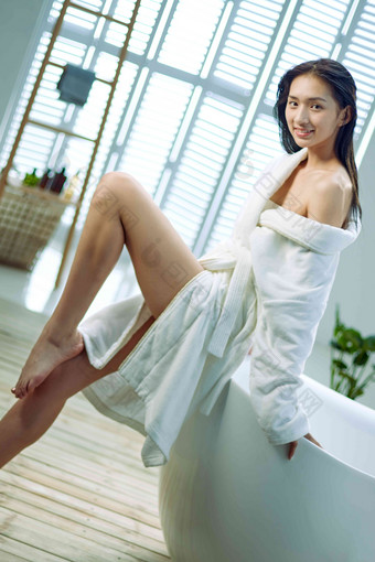 身穿浴袍的青年女人坐在浴缸边