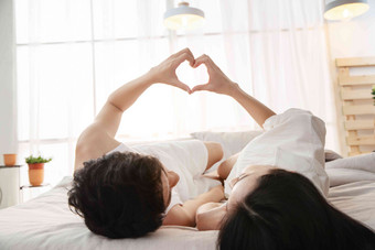快乐的年轻情侣躺在床上做心形手势