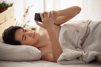 躺在床上玩手机的年轻男人