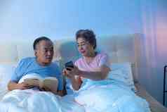 老年夫妇坐在床上看手机
