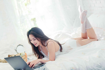 趴在床上使用笔记本电脑的年轻女人